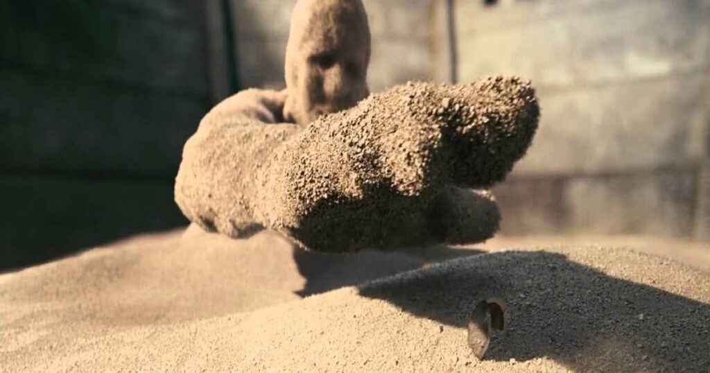 

A imagem mostra o personagem Flint Marko, o homem areia, tentando alcançar uma concha. 