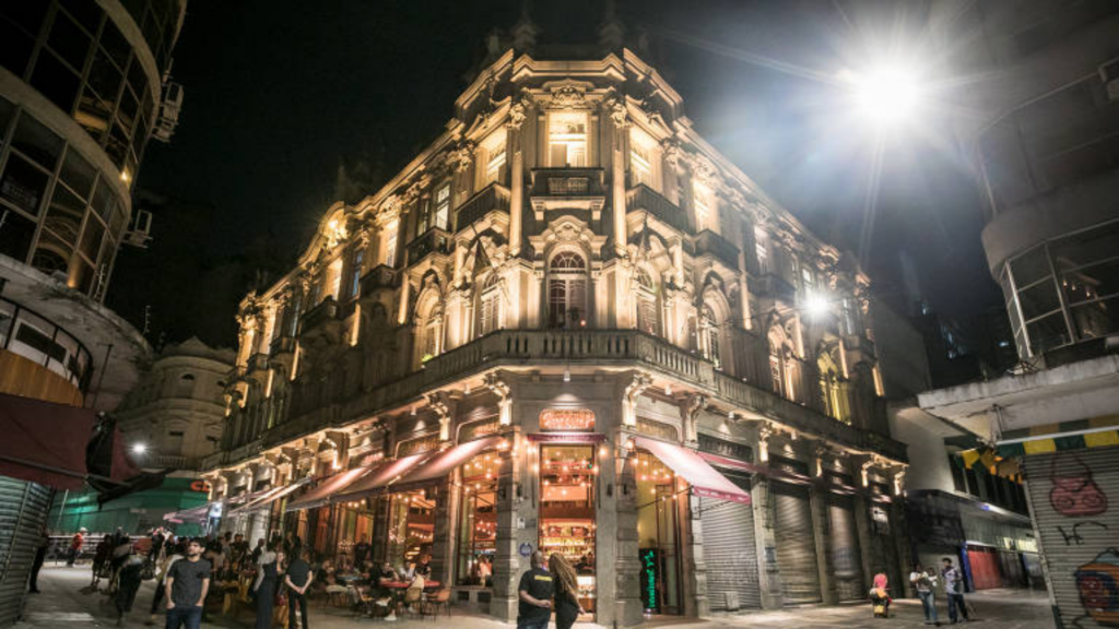Foto tirada da calçada que mostra a edificação à noite e iluminada da Casa de Francisca, com movimento.